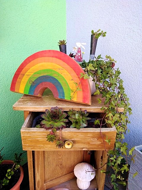 GrafikEin Regenbogenbild auf einem Nachttisch, der auch noch mit GrÃ¼n verziert ist und in einer Raumecke steht.