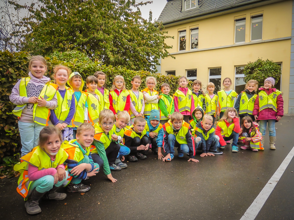 Schulklasse posiert mit Warnwesten vor dem Brunnen der Grundschule. 